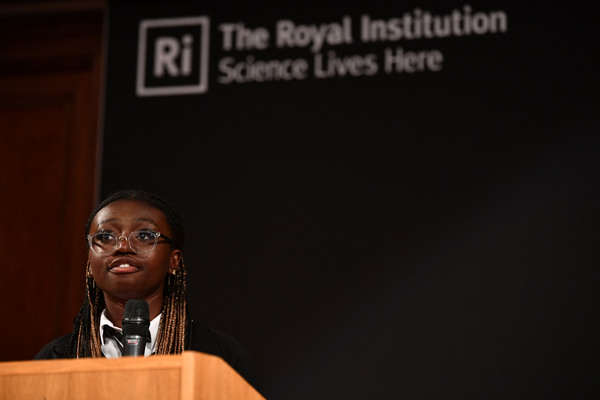 A young student stands in front The Royal Institution logo delivering her talk.