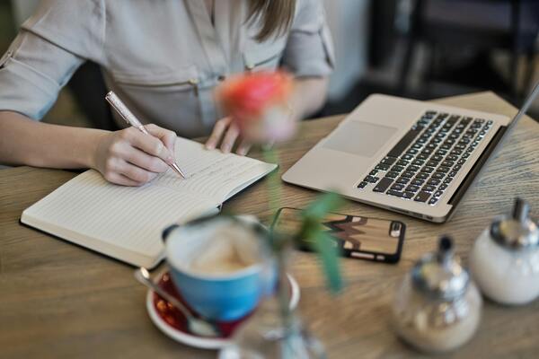 A computer, a notebook, a pen and a coffee over a table