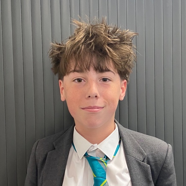 Head-and-shoulders portrait of Adrian Dredge, Young Science Writer Award 2026 winner, wearing a grey blazer, white shirt and turquoise striped tie against a grey background.