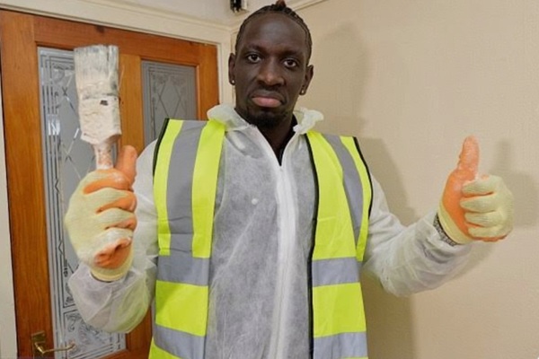 Man standing in room wearing a high vis jacket holding a paint brush