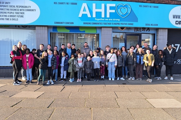 Group of children and young people in front of the office of An Hour for Others with large blue signage