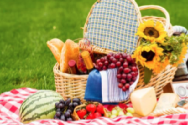 Photo of picnic basket with food and flowers on a blanket on the green grass