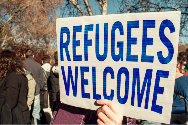 a  person sign with REFUGEES WELCOME in blue capitols outside
