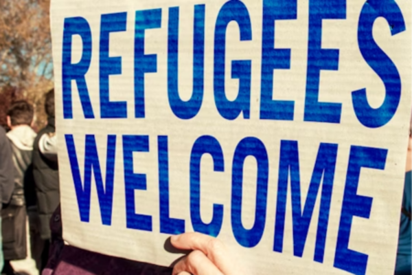 sign being held up that says 'refugees welcome' in blue capital letters 