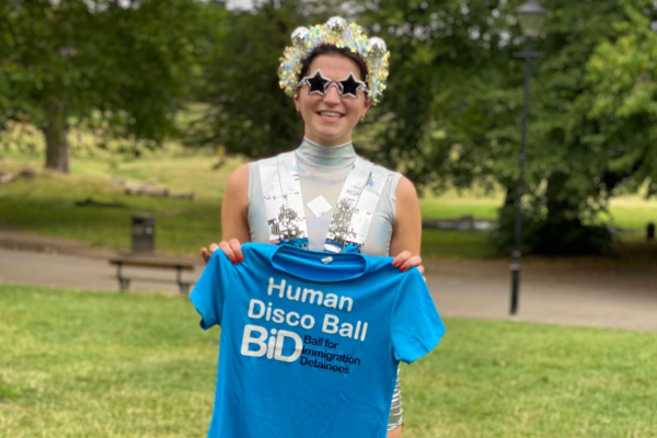 Freya is dressed up as a human disco ball holding a blue t-shirt with blue branding