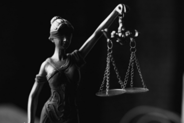 grey scale image of the lady of justice in front of a black background holding up a set of scales with her left hand