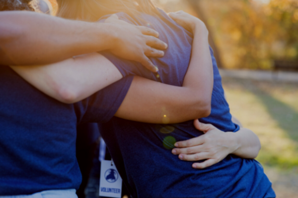 three people wearing blue t shirts hugging with their faces cut off 