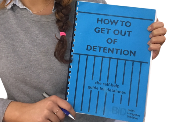 person wearing a grey sweater holding up a blue booklet which reads how to get out of detention