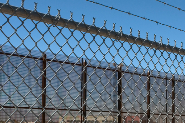 image of a grey fence against a blue sky. behind it there is another fence in the background