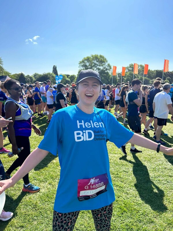 woman in  bright blue "BID" t-shirt standing on field with many other runners 