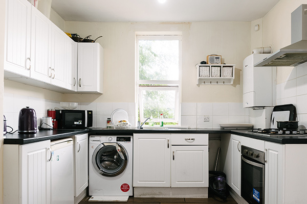 A photograph of a bright, homely kitchen, including a kettle, an oven and a washing machine.
