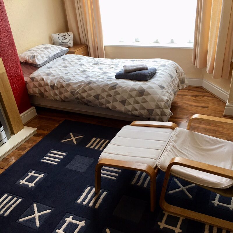 A warm and welcoming bedroom with a reclining chair, rug and a single bed.