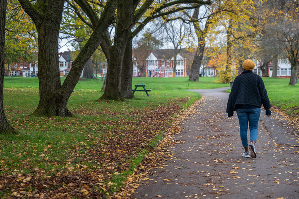 A woman walking alone, beneath Autumn trees.