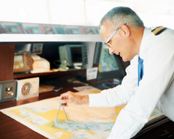 Photo of a captain leaning over a map plotting a course with a compass