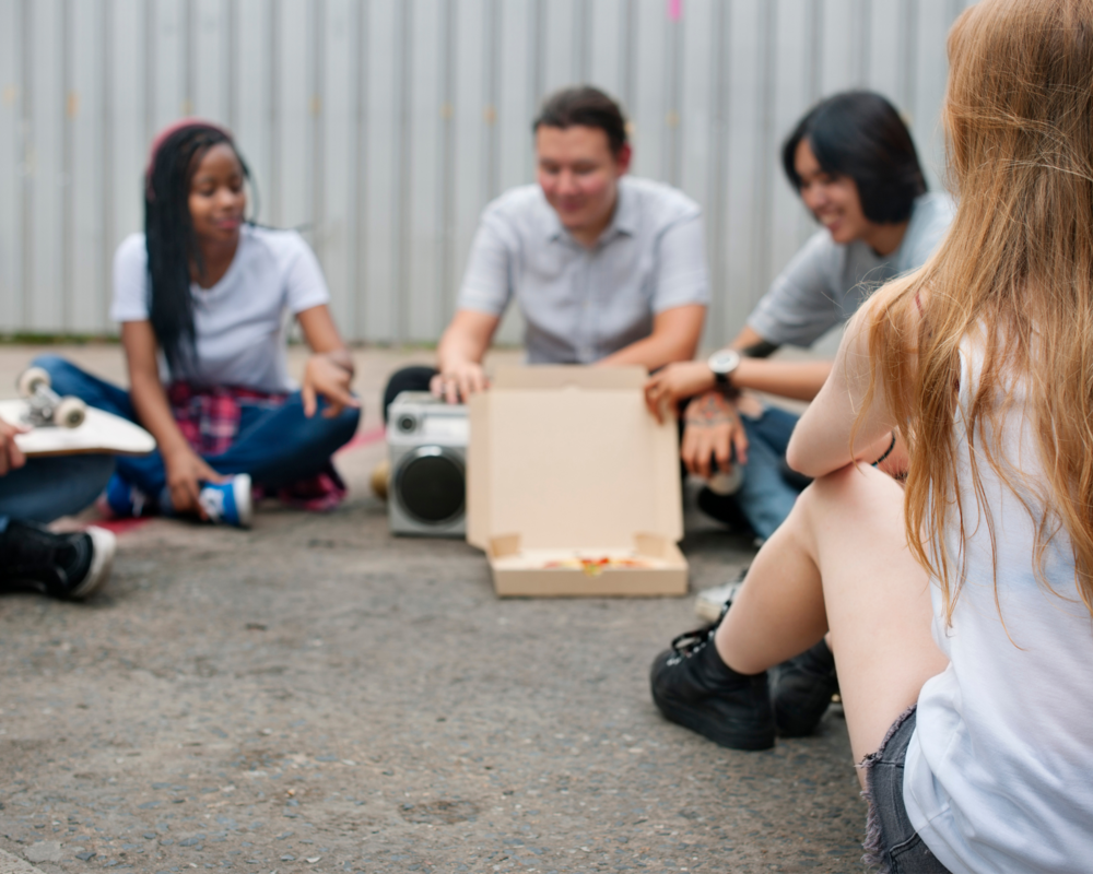 young people sitting on the ground sharing a pizza