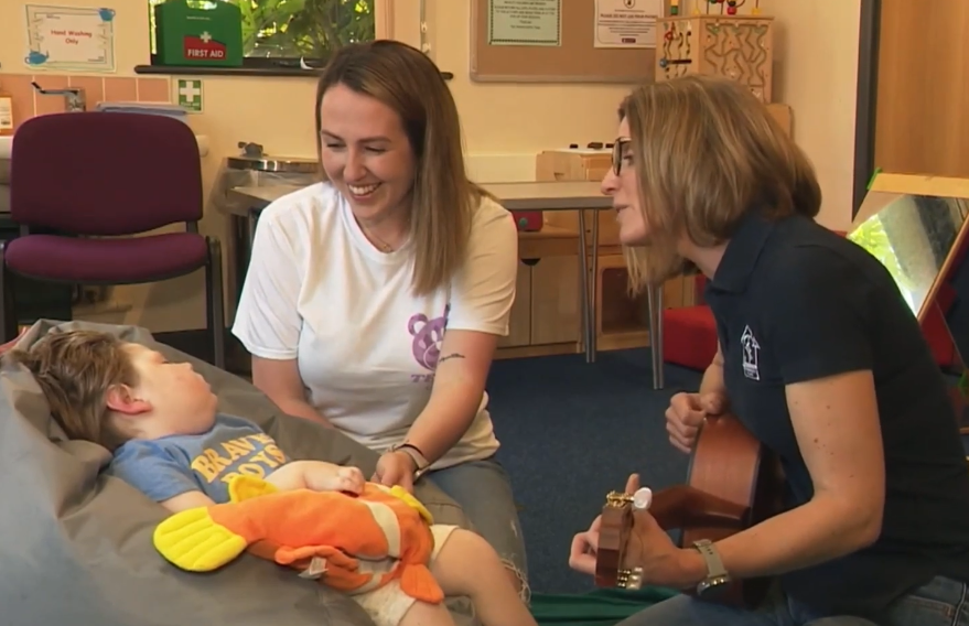 Two women pictured, one playing guitar to a young child.