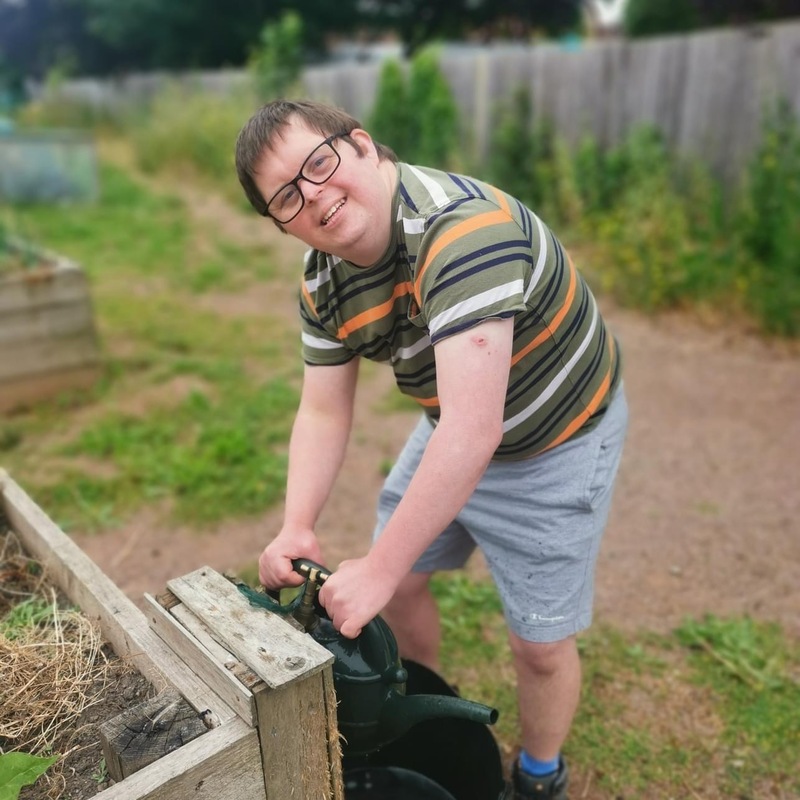 A young man wearing glasses filling a watering can