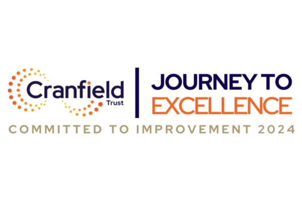 Cranfield Trust logo with Journey to Excellence written next to it, Journey to is written in navy blue and Excellence is written in orange. Underneath the logo are the words 'Committed to improvement 2024' in a gold colour