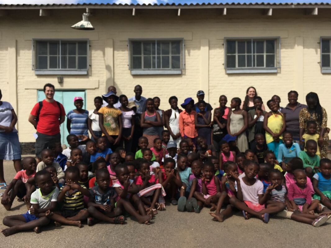 A large group of adults and children stood and sat in a group.