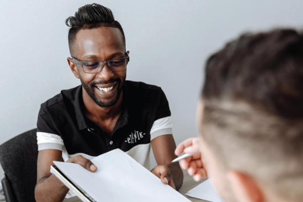 A man wearing glasses shows another man a document.