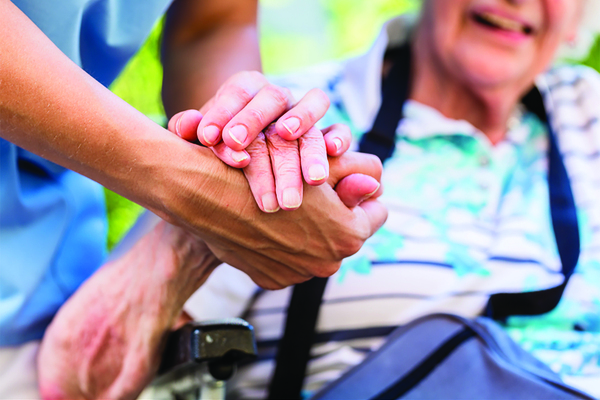 An older person holding the hand of a younger adult supporting them