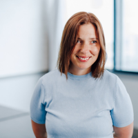Head and shoulders photo of Kim Page, a lady who shoulder length brown hair, smiling and looking slightly off camera. She is wearing a pale blue short sleeve top