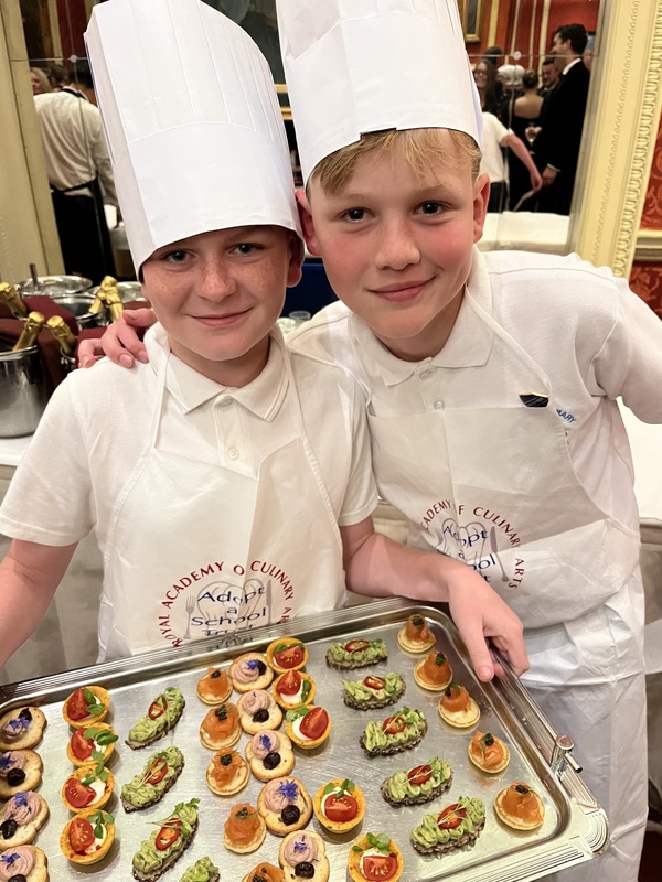Two smiling young boys wearing chefs hats with a tray of food