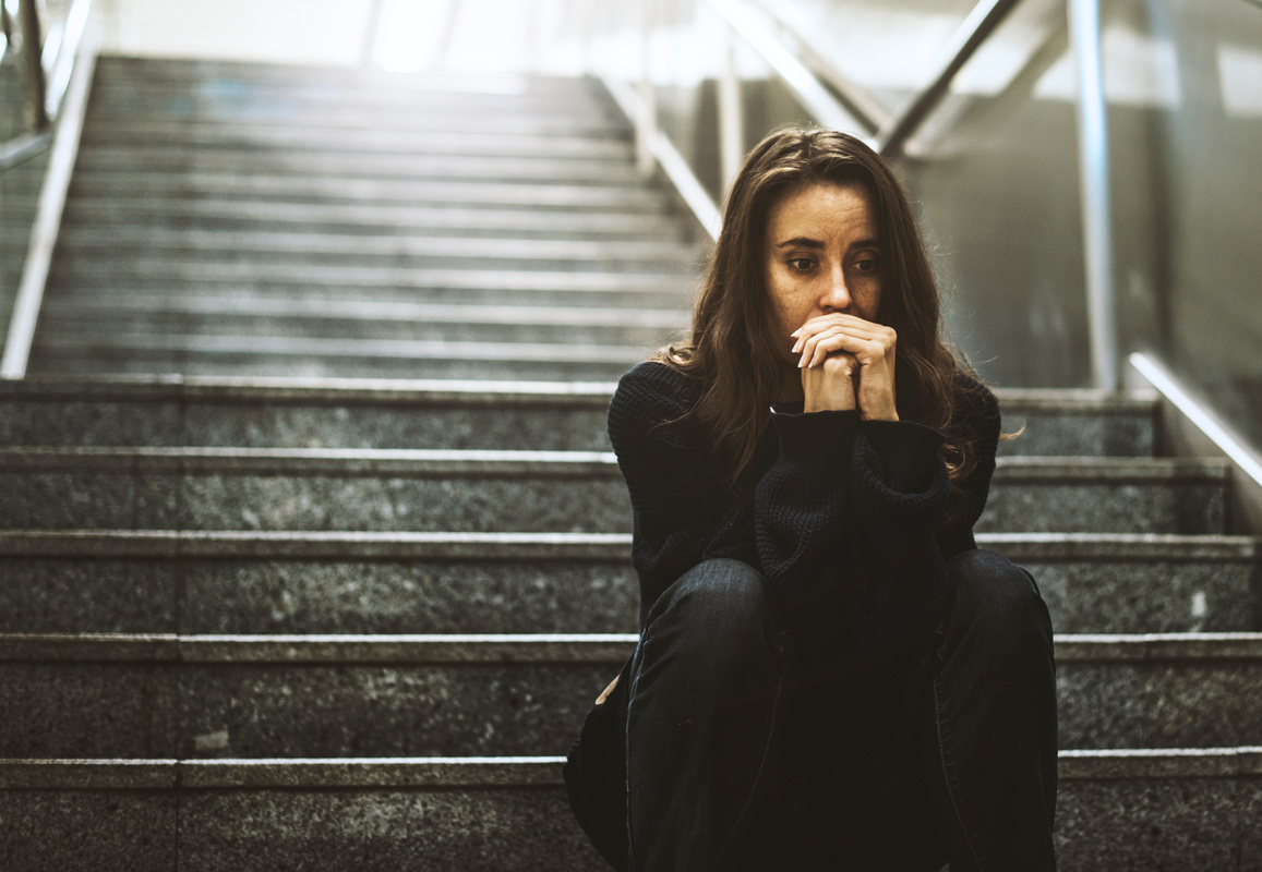 Image of a girl sat at the bottom of some steps looking pensive with her hands to her mouth
