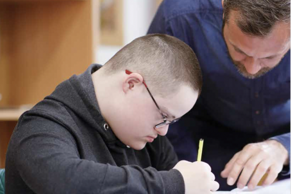 A man helps a young man with Down Syndrome with writing
