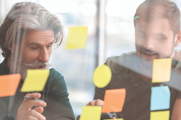Two men looking through a window with post it notes stuck on it