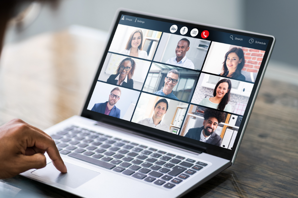 A finger points to a laptop showing a group meeting