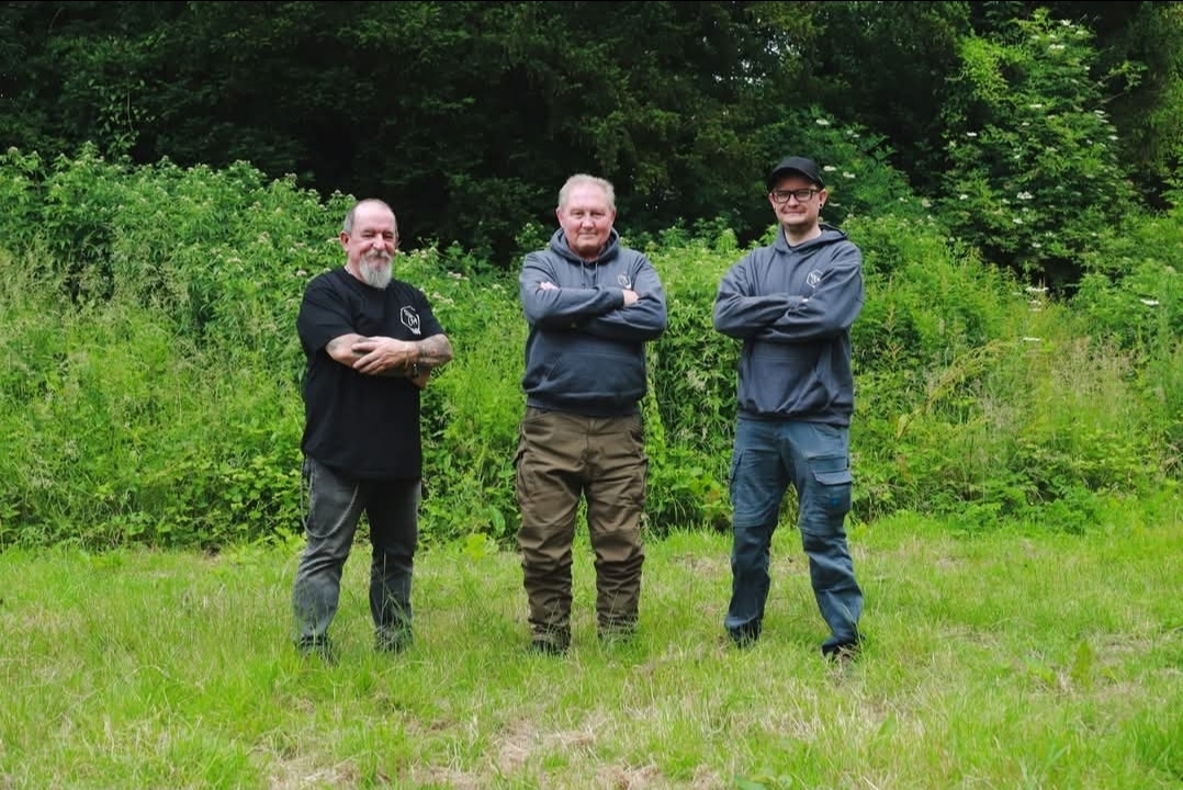 Image of three men standing on grass, all with folded arms
