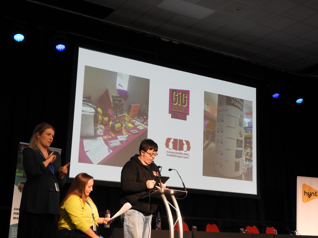 Three people on a stage with a presentation behind them