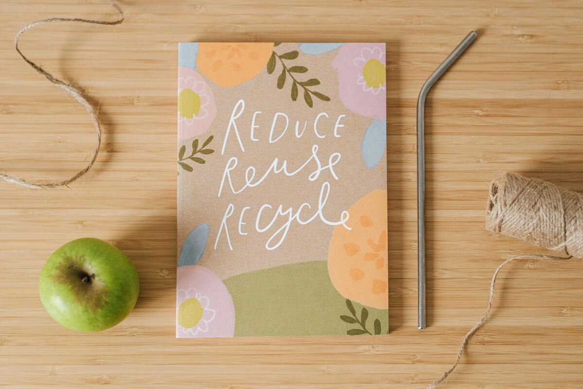 An apple, string, metal straw and notepad with Reduce Reuse Recycle on it