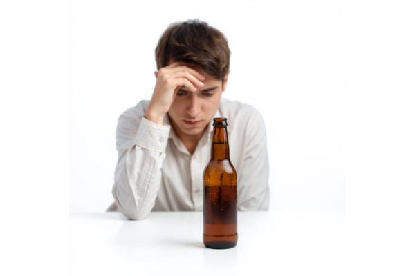 A man sits with his hand on his forehead like he is thinking. He his beside a bottle of beer.