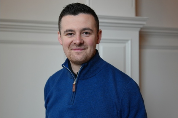 a photo of Sam smiling, wearing a blue jumper