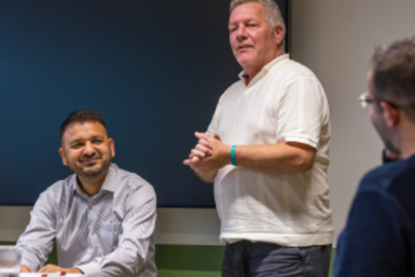 A A man smiling as another man, wearing a white t-shit speaks