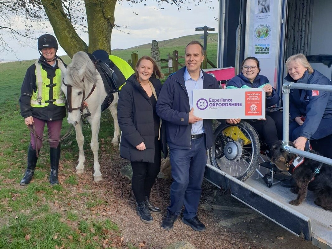 A group of people surrounding the Happiness Horsebox, a lovely white horse and a dog catch the eye most!