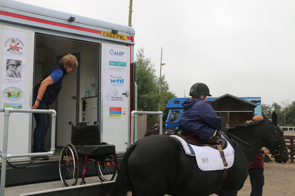 Rider on a black horse moves away from the Happiness Horsebox leaving her wheelchair on the ramp..