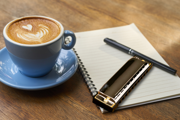 Coffee cup, harmonica, pen and notepad on table