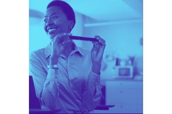 Photo of young black lady sat at office desk smiling and holding a harmonica