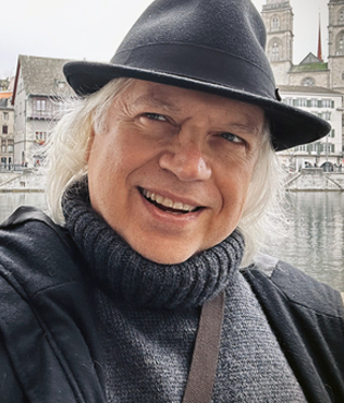 Image: Gene smiling wearing brimmed hat and scarf