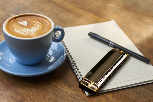 A coffee, a notebook and pencil, and a harmonica on a desktop