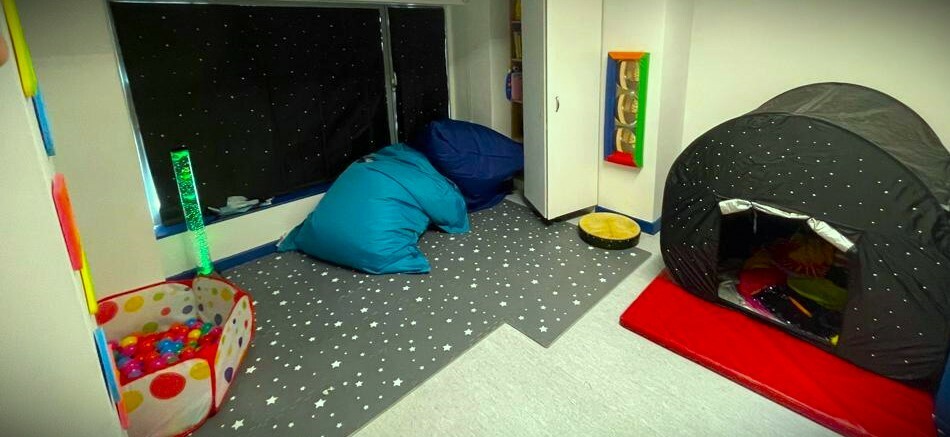 A cosy looking room with a tent, soft floooring, bean bags, a ball pit and blackout blinds