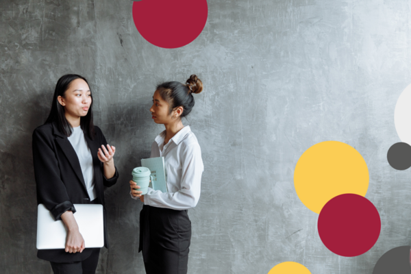 Two Women having a conversation in front of a grey wall.