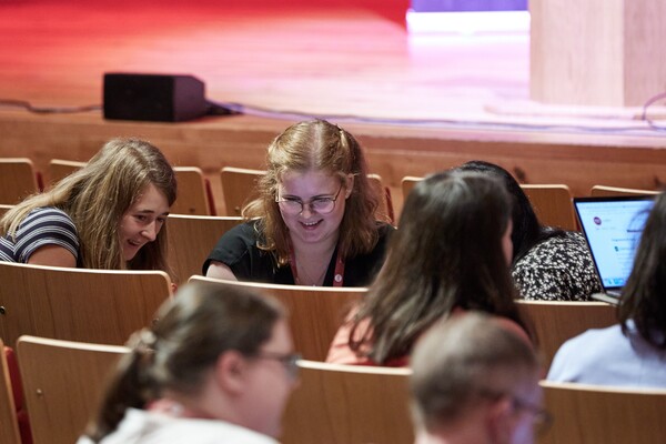 Women smile and laugh looking at a screen, sitting in theatre stalls 
