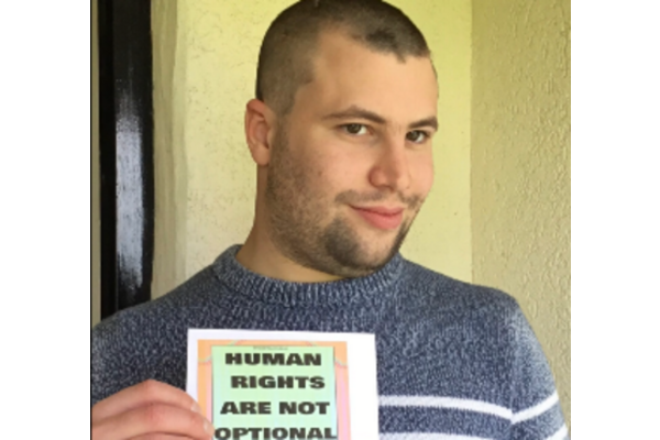 Photo of Charles holding a sign which reads "Human rights are not optional" 