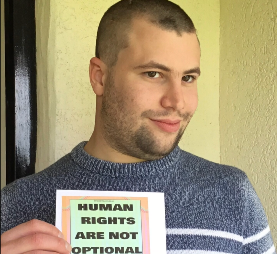 Photo of Charles holding a sign which reads "Human rights are not optional"