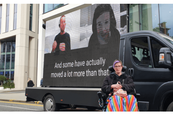 Disabled activist in front of a van displaying messages