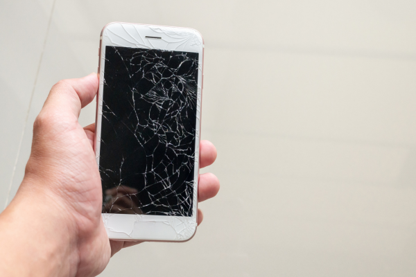 A hand holding a phone with a smashed screen